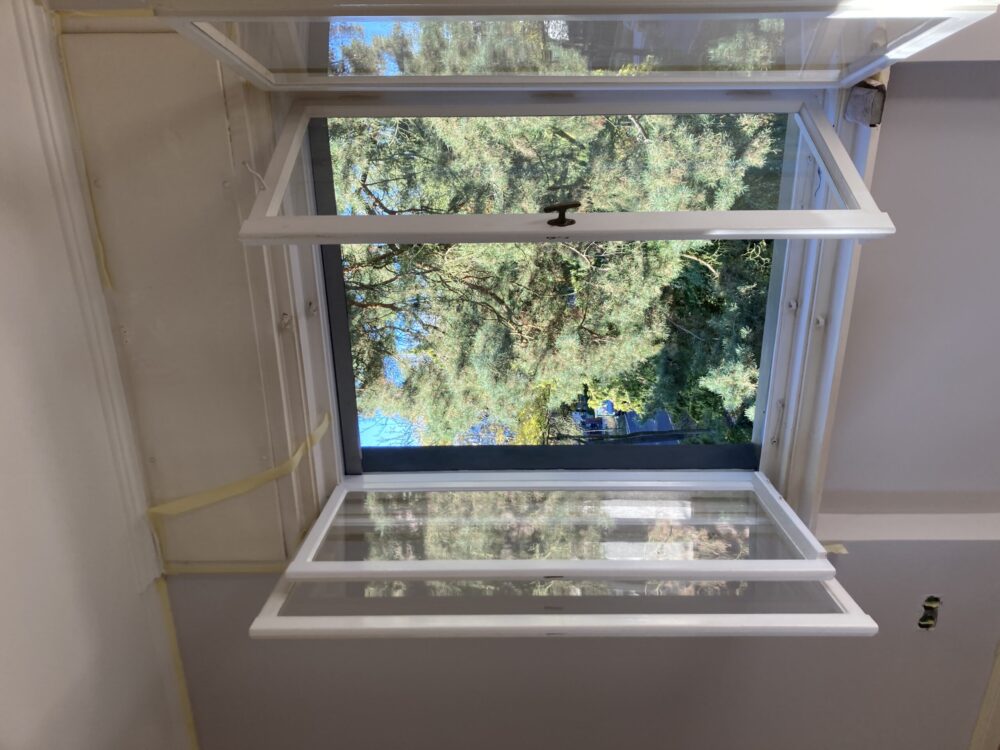 Offenes Fenster mit Blick auf grüne Bäume und blauen Himmel.