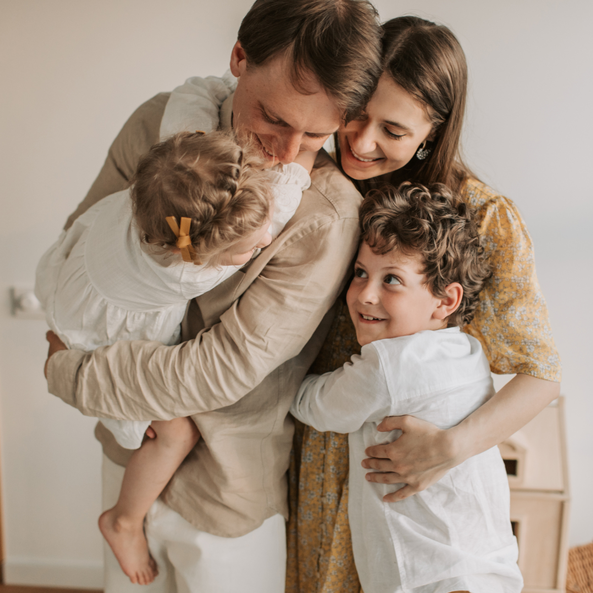 Familie mit zwei Kindern umarmt sich liebevoll in einem hellen Raum.