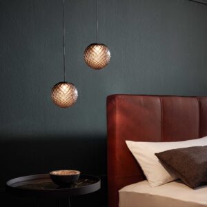 Zwei hängende Lampen über einem Nachttisch neben einem Bett mit braunem Kopfteil.