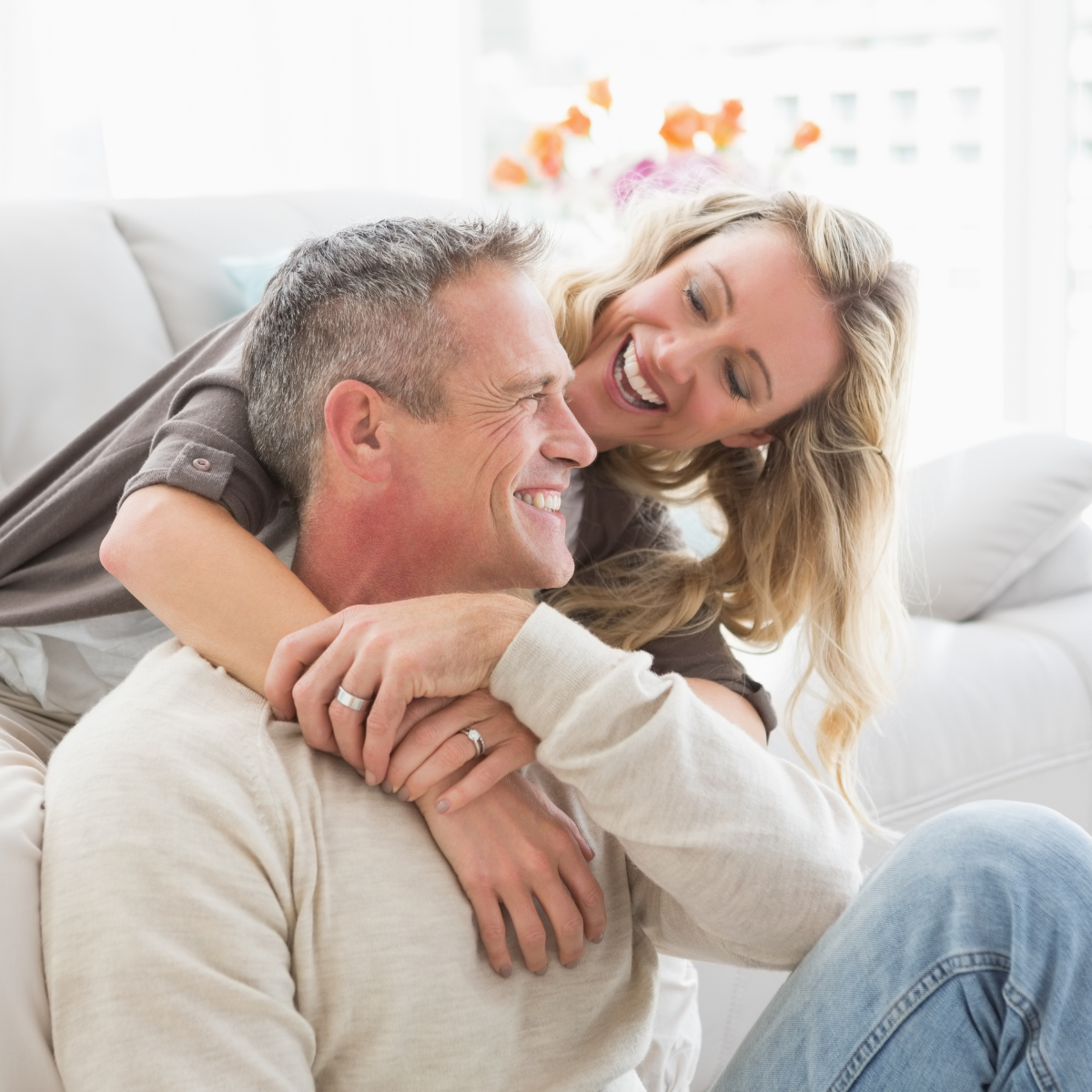 Glückliches Paar umarmt sich auf dem Sofa in hellem Wohnzimmer.