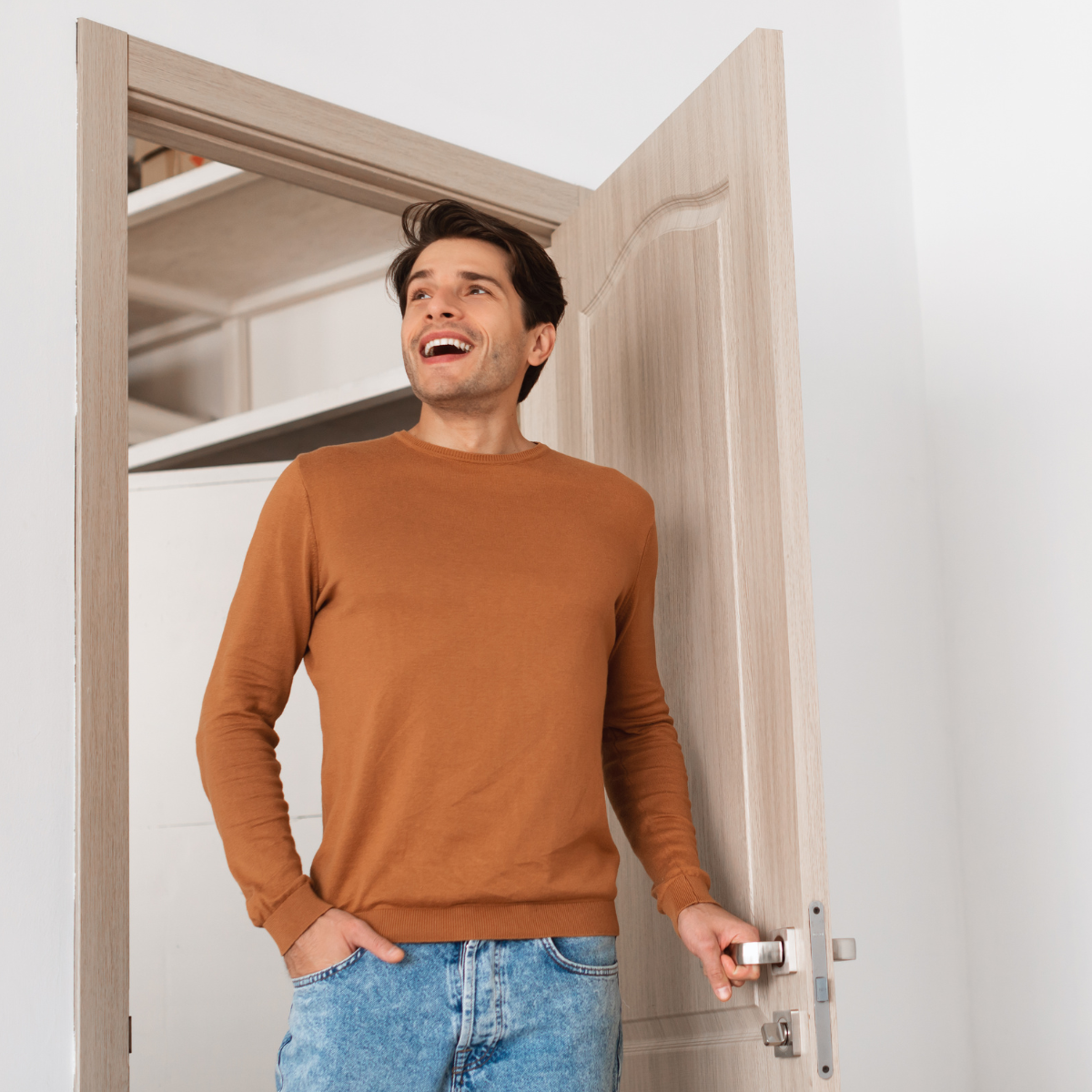 Mann in braunem Pullover öffnet eine Tür und lächelt.