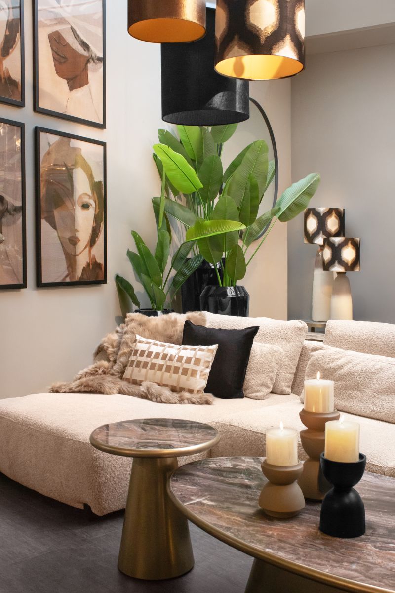 Gemütliches Wohnzimmer mit beiger Couch, dekorativen Kissen, Pflanzen, modernen Lampen und abstrakten Wandbildern.