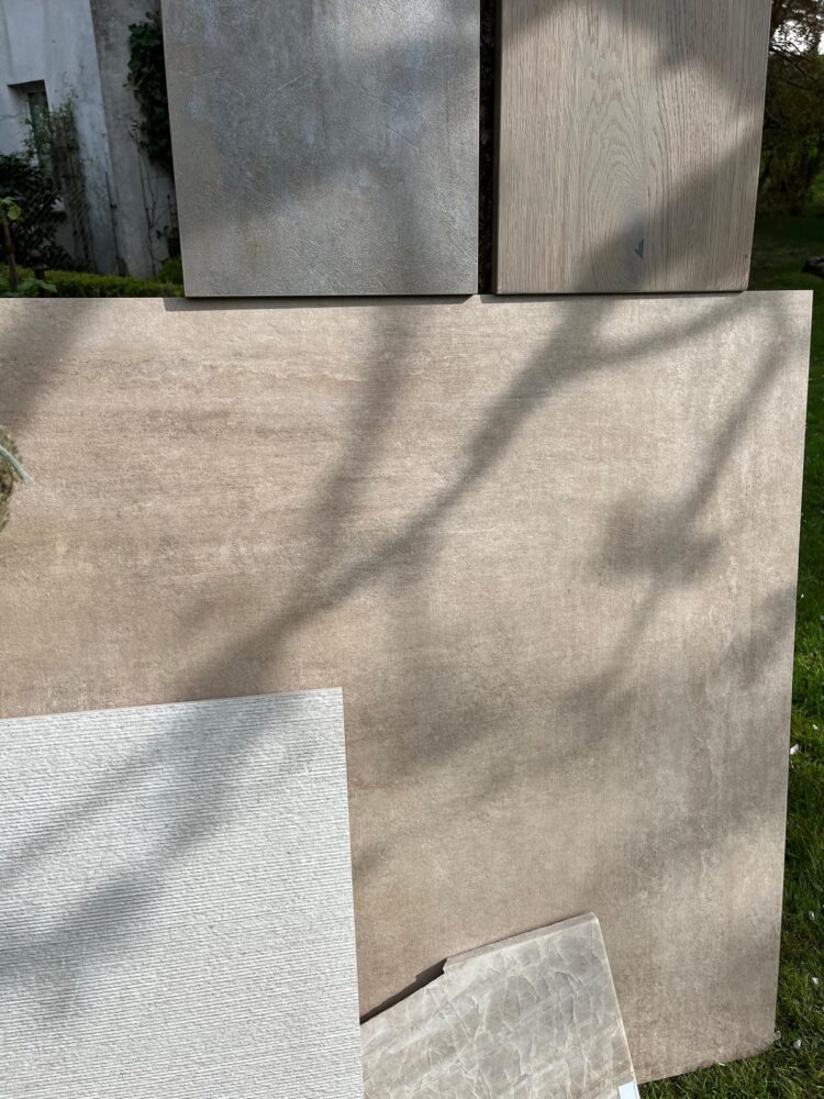 Verschiedene große Fliesen in neutralen Farbtönen auf Gras liegend, mit Schatten von Ästen.