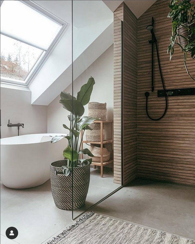 Modernes Badezimmer mit freistehender Badewanne, großer Pflanze in Korb, Holzregal und begehbarer Dusche unter Dachschräge.