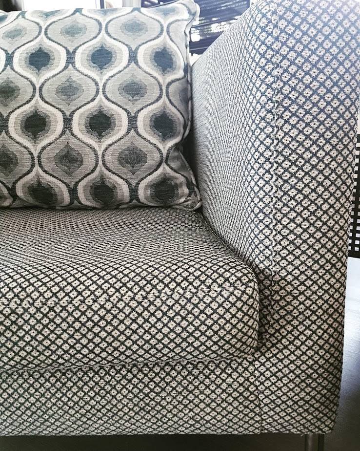 Nahaufnahme einer grauen Couch mit gemustertem Stoff und einem dekorativen Kissen.