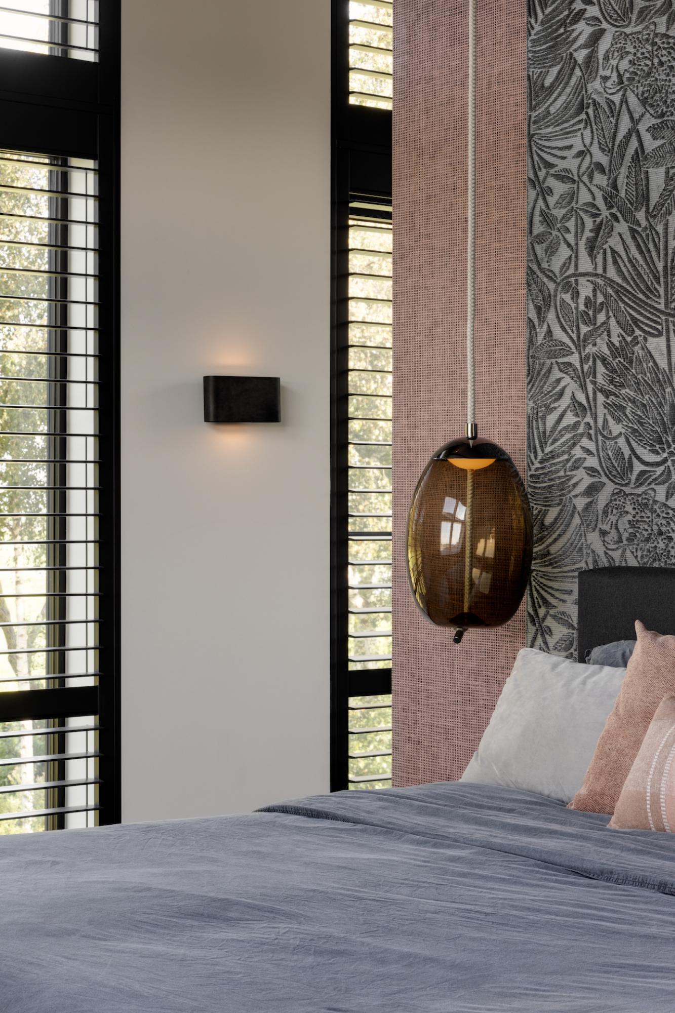 Modernes Schlafzimmer mit großem Fenster, grauem Bett und hängender brauner Lampe.