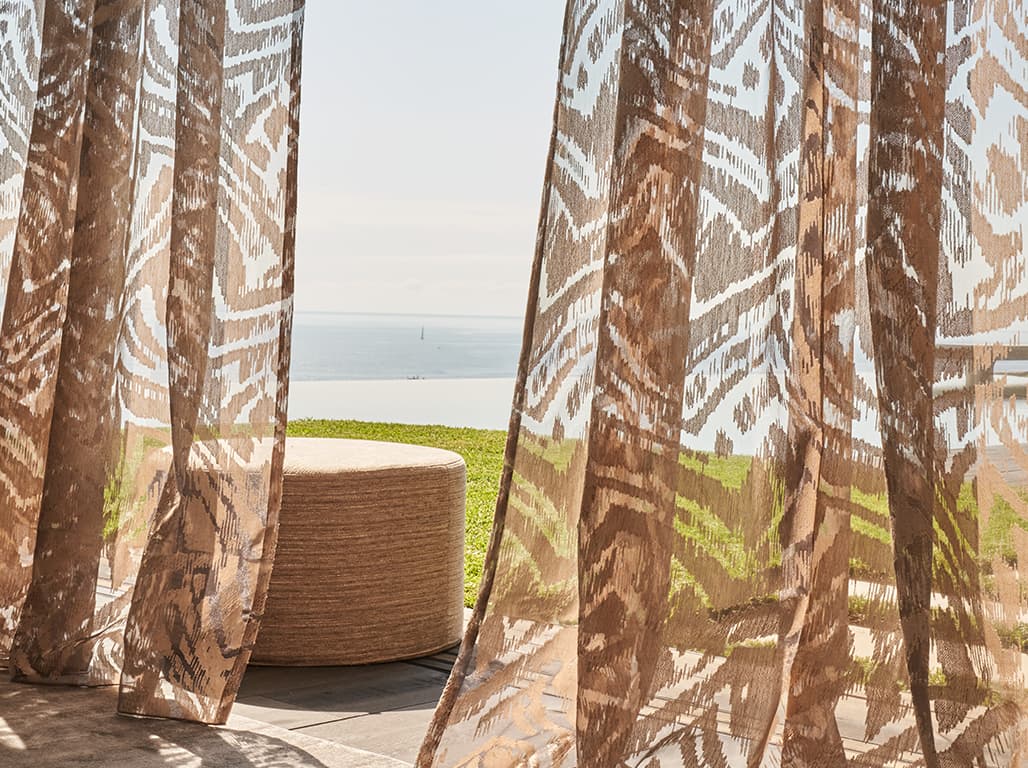 Durchscheinende Vorhänge vor einer Terrasse mit Blick auf Wasser und grünen Rasen.